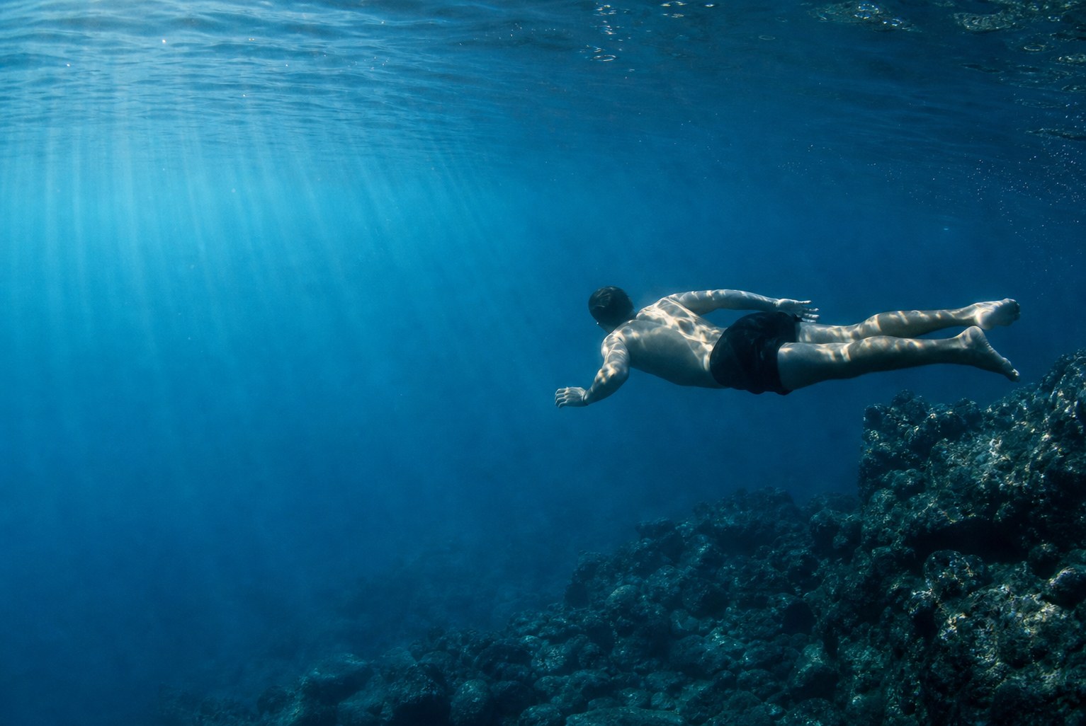Una persona flota bajo el agua atravesada por la luz