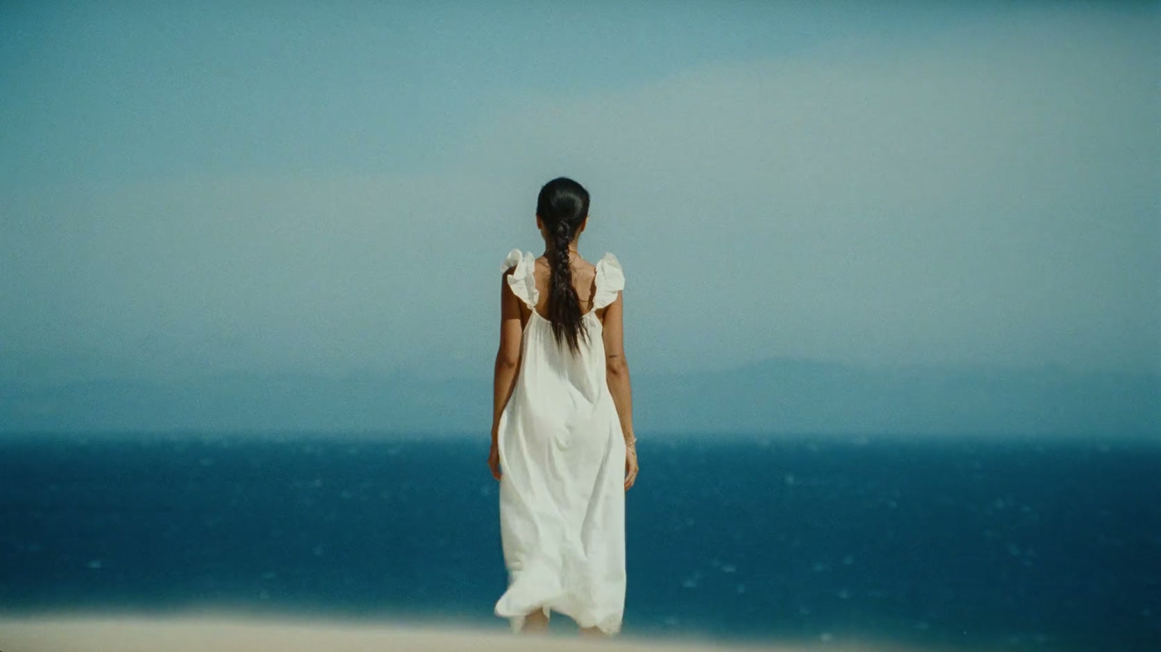 Una mujer vestida de blanco contempla el océano