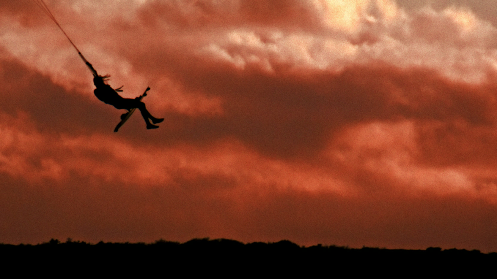 Una persona se balancea contra un cielo rojo